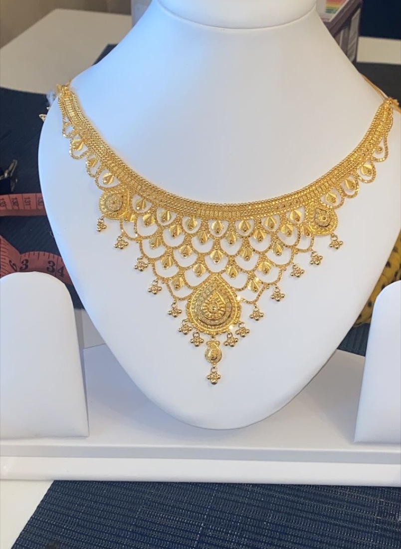 An intricate gold bridal necklace with a teardrop pendant on a display bust at Shivani Jewellers